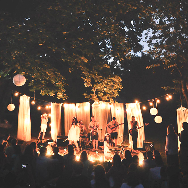 Wieczorny koncert muzyki medytacyjnej w Parku Ludowym. Zdjęcie z daleka pokazuje całą scenerię, podświetlonych dekoracji i zgromadzonych ludzi.